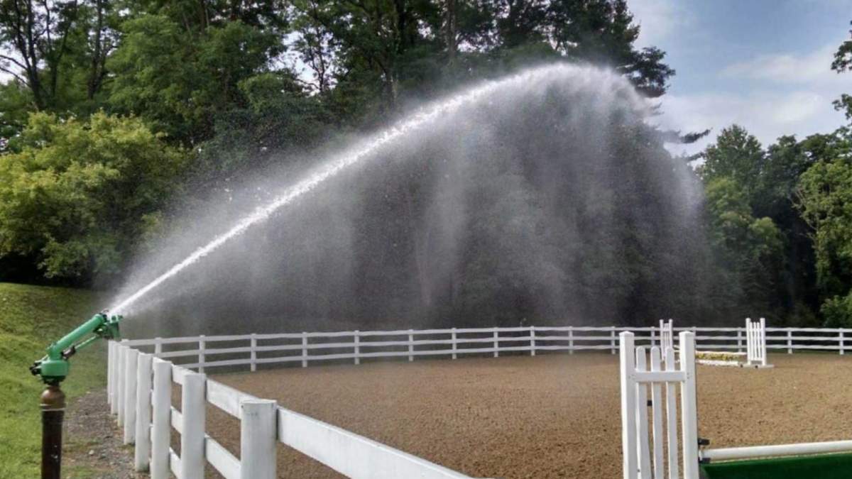 Big Sprinkler mounted sprinkler head spraying water on an equine exercise arena for dust suppression purposes